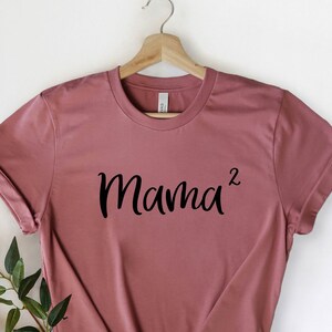 以下が含まれることがあります： マウブ色のTシャツに、黒い文字で「Mama^2」と書かれています。