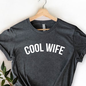 Puede incluir: Una camiseta gris oscuro con el texto "COOL WIFE" impreso en blanco en la parte delantera.
