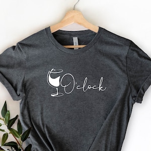May include: A dark gray t-shirt with a white wine glass graphic and the text "Wine o'clock".