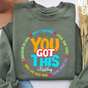 May include: Green sweatshirt with a motivational quote in a circle: "I believe in you, don't stress, rock the test, do your best, you got this, #Testday".