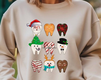 May include: A beige sweatshirt with a Christmas-themed design featuring nine cartoon teeth wearing various holiday accessories, including a Santa hat, a Christmas tree, candy canes, a snowman hat, reindeer antlers, and a gingerbread man.