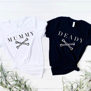 May include: Two t-shirts, one white and one black, with the words "MUMMY" and "DEADLY" printed on them. Both shirts feature a pair of crossed bones.