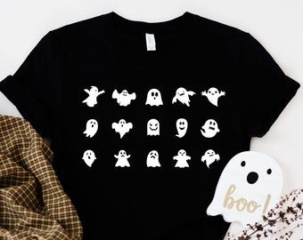 May include: A black t-shirt featuring a white graphic of various ghosts in different poses. The shirt has a crew neck and short sleeves. A white ghost with the word "boo!" is in the bottom right corner of the image.