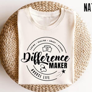 May include: A white t-shirt with a black circle graphic that says "Caring - Healing - Smart - Strong" and "Difference Maker #NurseLife".