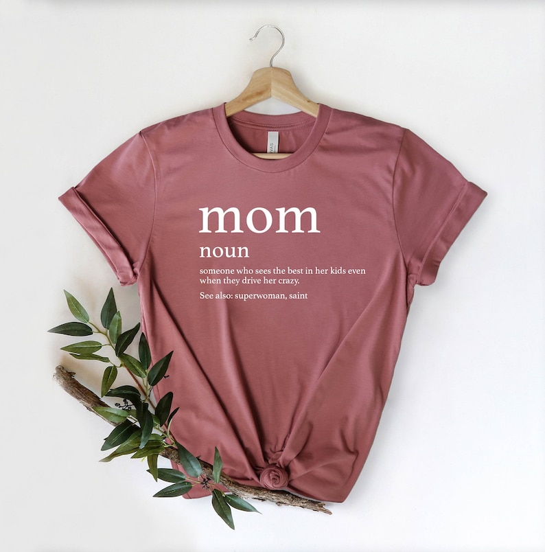 May include: A maroon t-shirt with the word "mom" in white text, defined as "someone who sees the best in her kids even when they drive her crazy. See also: superwoman, saint."