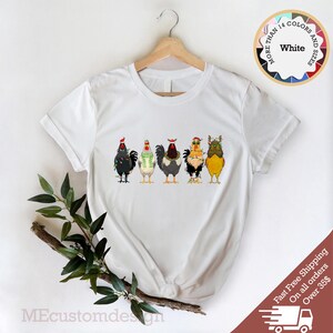May include: White t-shirt with a graphic of five chickens wearing Christmas hats and lights. The text "More Than 14 Colors and Sizes" is on a circle in the upper right corner of the image. The text "White" is in the center of the circle.