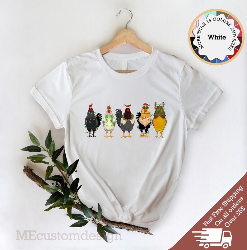May include: White t-shirt with a graphic of five chickens wearing Christmas hats and lights. The text "More Than 14 Colors and Sizes" is on a circle in the upper right corner of the image. The text "White" is in the center of the circle.