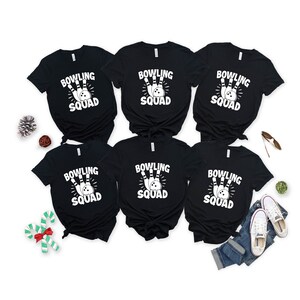 May include: Six black t-shirts with white text that reads "Bowling Squad" and a graphic of a bowling ball and pins.