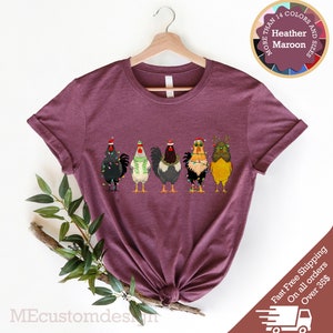 May include: A heather maroon t-shirt with a graphic of five chickens wearing Santa hats and Christmas lights. The text "More Than 14 Colors and Sizes" is in a circle above the chickens.