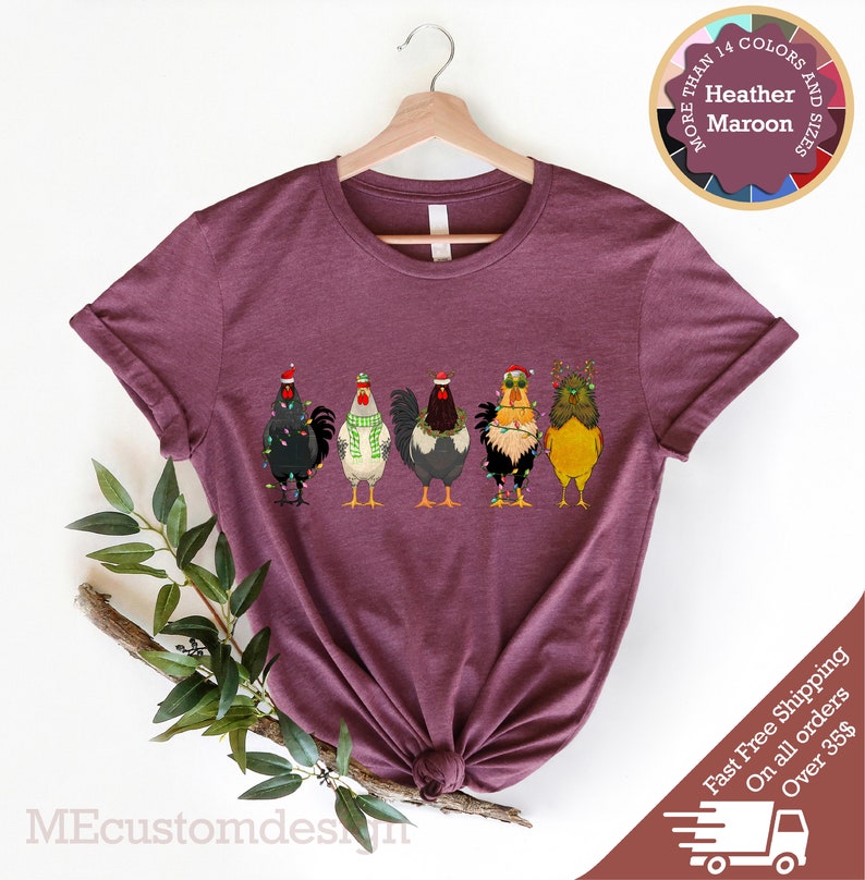 May include: A heather maroon t-shirt with a graphic of five chickens wearing Santa hats and Christmas lights. The text "More Than 14 Colors and Sizes" is in a circle above the chickens.