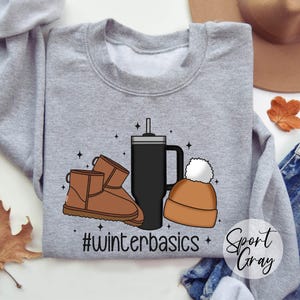 May include: Gray sweatshirt with a graphic design of a coffee cup, a beanie, and a pair of brown boots. The text "#winterbasics" is printed on the sweatshirt.
