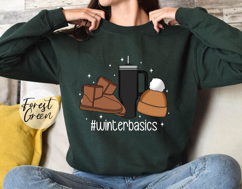 May include: Forest green sweatshirt with a graphic design of a pair of brown Ugg boots, a black travel mug, and a brown beanie with a white pom pom. The text "#winterbasics" is printed below the graphic.