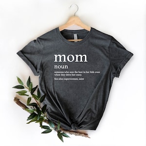 May include: A dark gray t-shirt with the word "mom" defined as "someone who sees the best in her kids even when they drive her crazy." The definition also includes "See also: superwoman, saint."