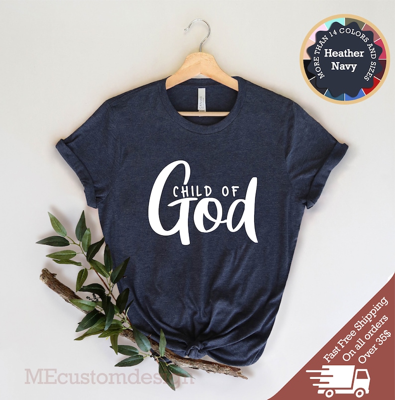 May include: A navy blue t-shirt with the text "CHILD OF GOD" in white lettering. The shirt is hanging on a wooden hanger against a white background.