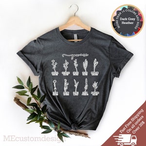 May include: Dark grey t-shirt with a white graphic design featuring a floral illustration and the text "you are" followed by a list of positive words. The words are: beautiful, victorious, enough, created, never alone, strong, amazing, capable, chosen, always loved.