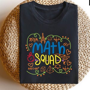 May include: Black t-shirt with a colorful graphic design featuring the text "Math Squad" surrounded by math symbols and equations, including pi, a compass, a protractor, and a triangle.