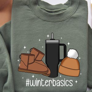 May include: A green sweatshirt with a graphic design of a pair of brown boots, a black travel mug with a straw, and a brown beanie with a white pom pom. The text "#winterbasics" is printed below the graphic.