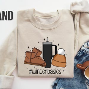 May include: A beige sweatshirt with a graphic design of a coffee cup, a beanie, and a pair of brown boots. The text "#winterbasics" is printed below the graphic.
