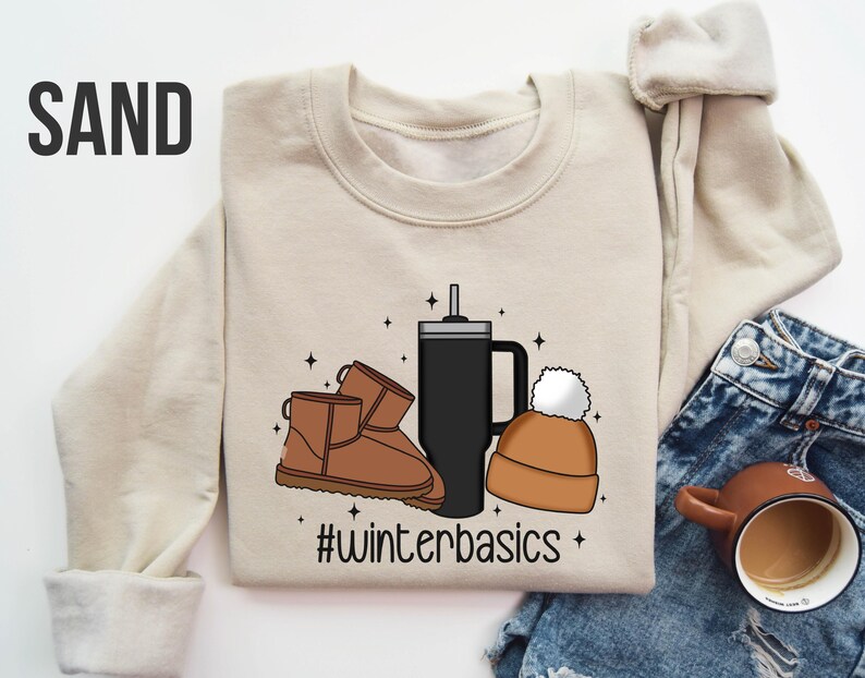 May include: A beige sweatshirt with a graphic design of a coffee cup, a beanie, and a pair of brown boots. The text "#winterbasics" is printed below the graphic.