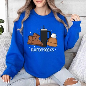 May include: A royal blue sweatshirt with a graphic design of a coffee cup, a beanie, and a pair of brown winter boots. The text "#winterbasics" is printed below the graphic.