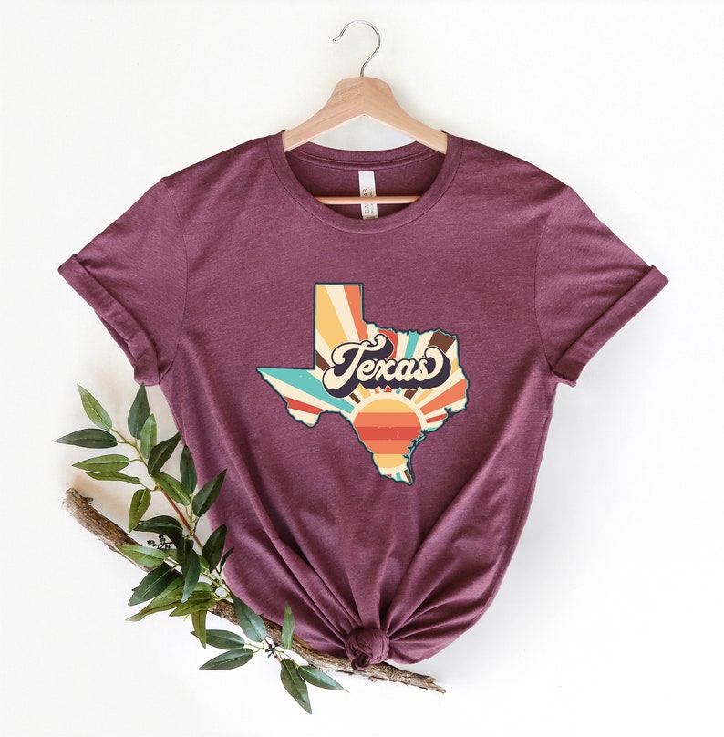 May include: A maroon t-shirt with a vintage-style graphic of the state of Texas with a sunburst design and the word "Texas" in a retro font.
