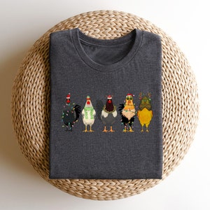 May include: A dark gray t-shirt with a design of five chickens wearing Christmas hats and lights. The chickens are in a line, facing forward.