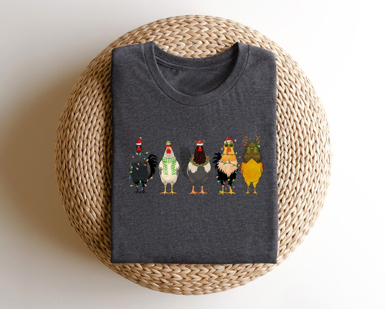 May include: A dark gray t-shirt with a design of five chickens wearing Christmas hats and lights. The chickens are in a line, facing forward.