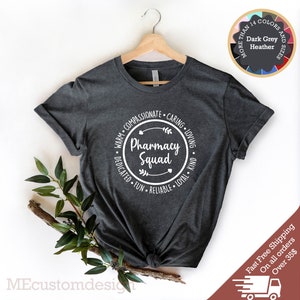 May include: Dark heather grey t-shirt with a white circle graphic that says "Pharmacy Squad" surrounded by the words "Warm, Compassionate, Caring, Loving, Dedicated, Fun, Reliable, Loyal, Kind".