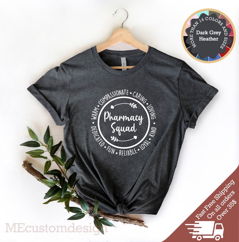 May include: Dark heather grey t-shirt with a white circle graphic that says "Pharmacy Squad" surrounded by the words "Warm, Compassionate, Caring, Loving, Dedicated, Fun, Reliable, Loyal, Kind".