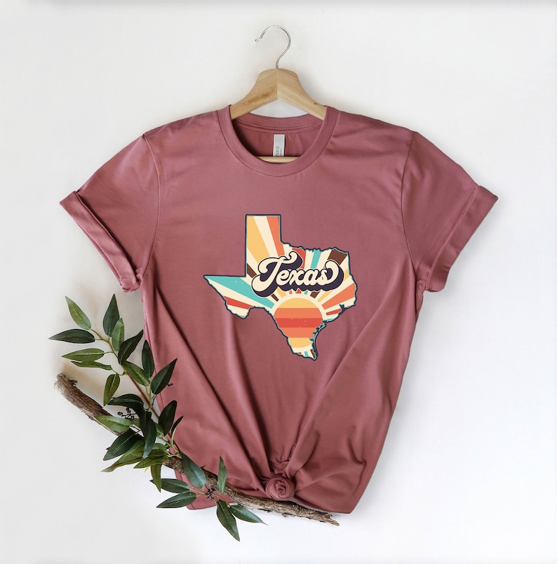 May include: A maroon t-shirt with a vintage-style graphic of the state of Texas with a sunburst design and the word "Texas" in a retro font.