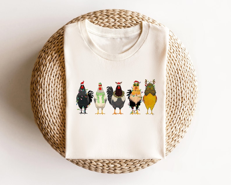 May include: A white t-shirt with a graphic of five chickens wearing Christmas hats and lights. The chickens are in a row, facing forward. The background is white.