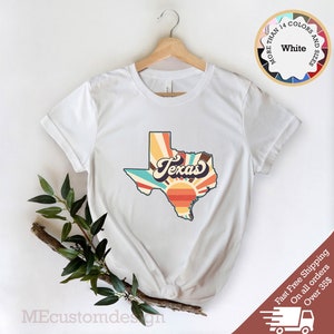 May include: White t-shirt with a retro-style graphic of the state of Texas with a sunrise and the word "Texas" in a vintage font.