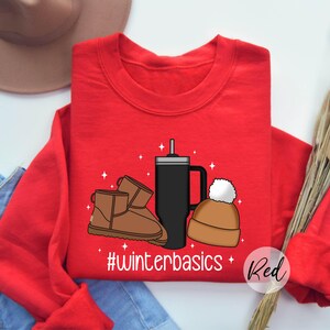 May include: Red sweatshirt with a graphic design of a coffee cup, a pair of brown boots, and a winter hat. The text "#winterbasics" is printed below the graphic. The word "Red" is written in white text on a red circle in the bottom right corner of the image.