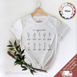 May include: White t-shirt with a floral design and the text "you are" with bible verses listed below each flower.