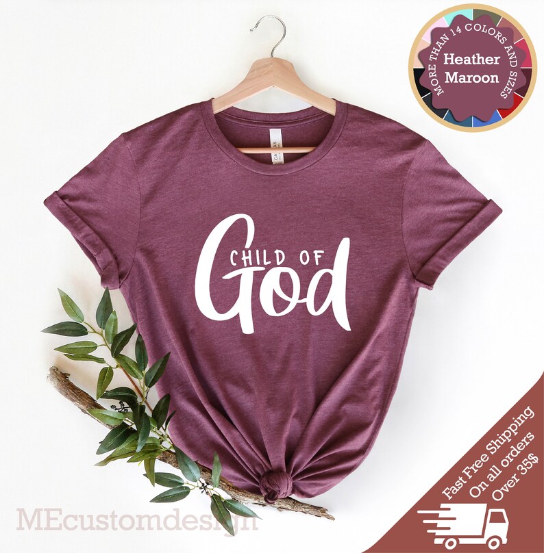 May include: A maroon t-shirt with the text "CHILD OF GOD" in white lettering. The shirt is hanging on a wooden hanger.