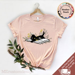 May include: A black cat reading a book surrounded by flowers. The cat is lying on the book with its head resting on the page. The flowers are in shades of yellow and white.