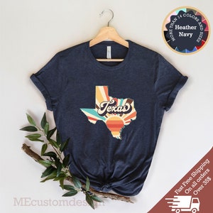 May include: A navy blue t-shirt with a retro-style graphic of the state of Texas with a sunset and the word "Texas" in a vintage font.