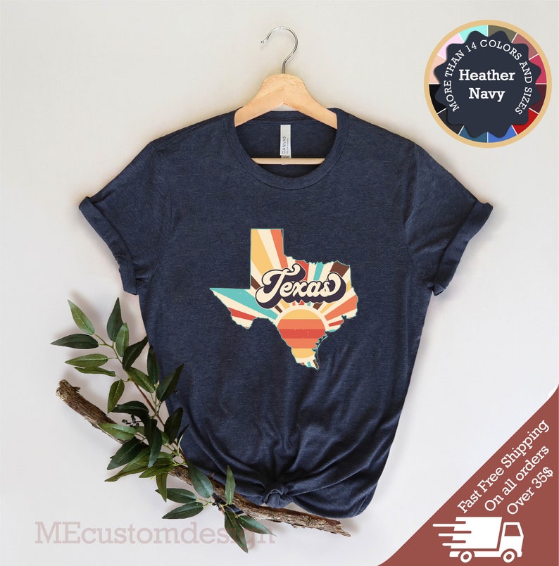 May include: A navy blue t-shirt with a retro-style graphic of the state of Texas with a sunset and the word "Texas" in a vintage font.