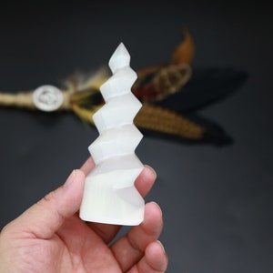 May include: White selenite crystal carved into a spiral shape. The crystal is smooth and polished, with a slightly translucent appearance.