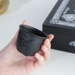 May include: Black ceramic cauldron with a pentagram and triple moon design.