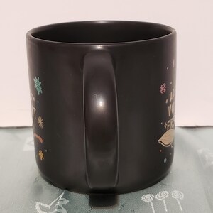 May include: Black ceramic mug with a white handle and colorful designs. The mug has the text "What you do for yourself, you do for your friends." printed on it.