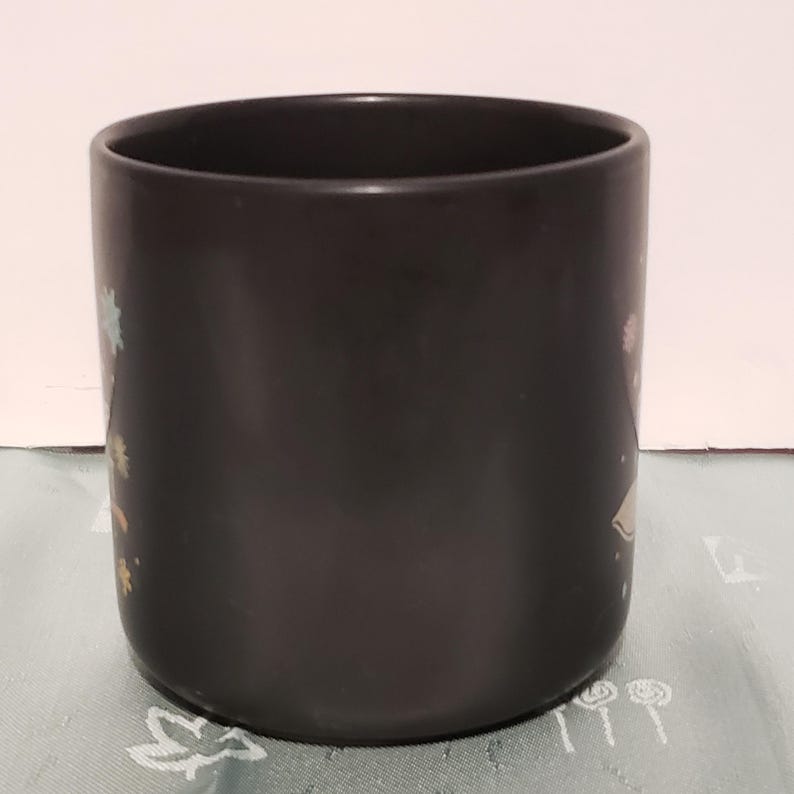 May include: A black ceramic mug with a colorful design. The mug has a wide rim and a rounded bottom.