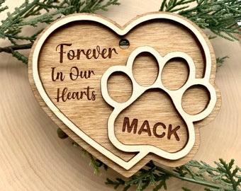 Könnte beinhalten: Hölzerner herzförmiger Anhänger mit einem Pfotenabdruck-Ausschnitt. Der Anhänger ist mit dem Text "Forever In Our Hearts" und dem Namen "Mack" graviert.