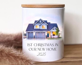 Könnte beinhalten: Weißer Kerzenhalter aus Keramik mit Bambusdeckel. Der Kerzenhalter zeigt eine Hausillustration mit blauem Dach und dem Text "1st Christmas in Our New Home 2025".