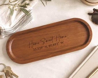 May include: An oval wooden tray with a smooth finish, featuring the engraved text "Home Sweet Home" followed by the coordinates "35.539° N, 80.893° W" centered on the surface. The tray has a raised rim and a natural brown wood grain texture.