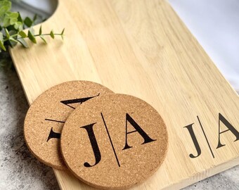 Könnte beinhalten: Ein Holzbrett zum Schneiden mit zwei Korkuntersetzern. Die Untersetzer haben die Initialen "J|A" aufgedruckt. Das Schneidebrett hat ebenfalls die Initialen "J|A" aufgedruckt.