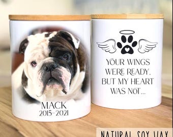 Könnte beinhalten: Zwei weiße Keramikkerzen mit Bambusdeckeln. Eine Kerze zeigt ein Bulldoggenporträt mit dem Namen "MACK" und den Daten "2015-2021". Die andere Kerze hat einen Pfotenabdruck mit Flügeln und dem Text "YOUR WINGS WERE READY, BUT MY HEART WAS NOT..."