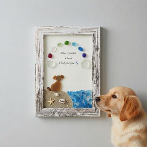 Könnte beinhalten: Ein gerahmtes Wandbild mit einem Hund aus braunem Meerglas, der auf einem Strand aus Sand und Muscheln sitzt, mit Wasser aus blauem Meerglas und einem Regenbogen aus Meerglasstücken. Der Text lautet: When I needed a hand, I had your paw.