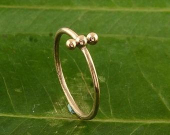 May include: A gold-colored ring with three small, round beads. The ring has a delicate, curved design. The ring is set against a green leaf background. The text "Danicajewelleryshop" is visible at the bottom of the image.