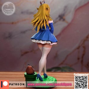 K&ouml;nnte beinhalten: Figur einer Figur mit langen blonden Haaren, die ein blaues Kleid mit wei&szlig;em Besatz und blaue Abs&auml;tze tr&auml;gt. Die Figur steht auf einer gr&uuml;nen Basis mit einem braunen Pilz und einem gr&uuml;nen Rohr. Die Figur hat eine Krone auf dem Kopf. Der Text "Peach Figure" ist sichtbar.